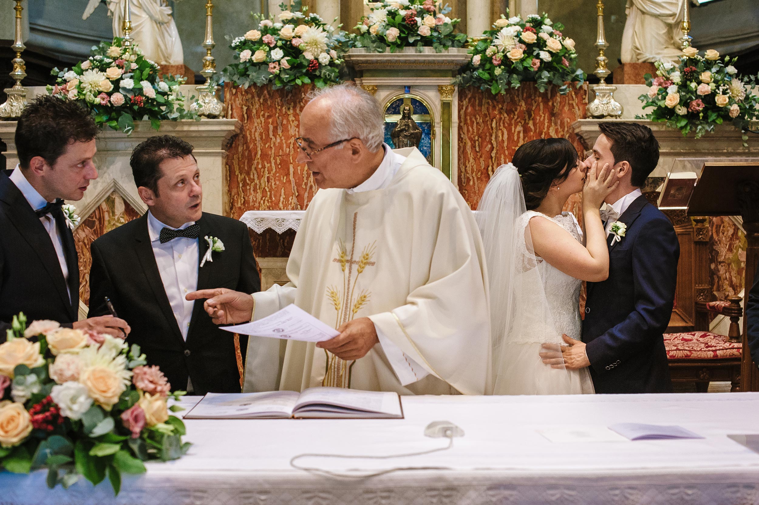 the bride kisses the groom in church while witnesses wait to sign