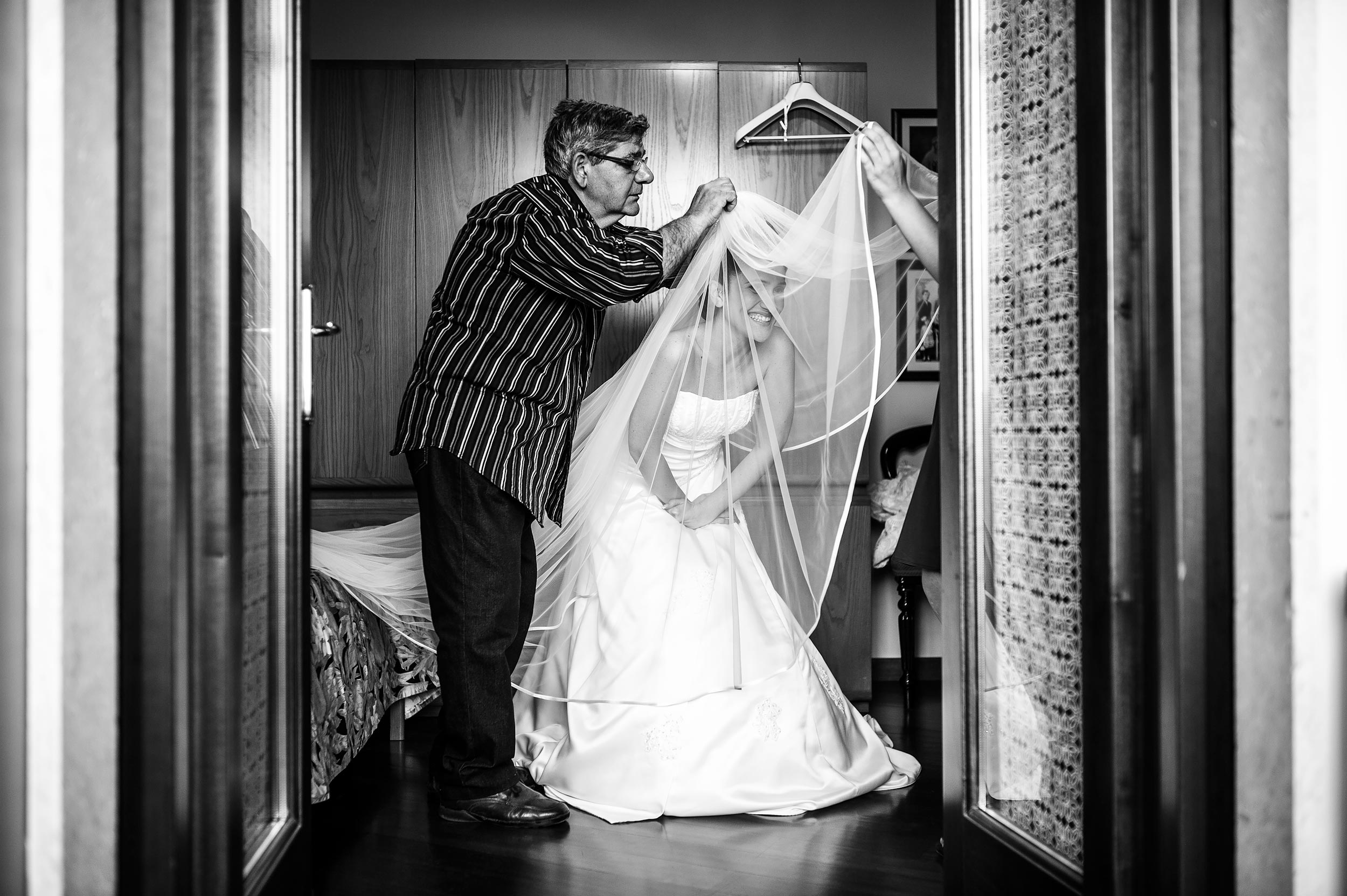 bride getting ready helped by a man putting the veil on black and white wedding photography