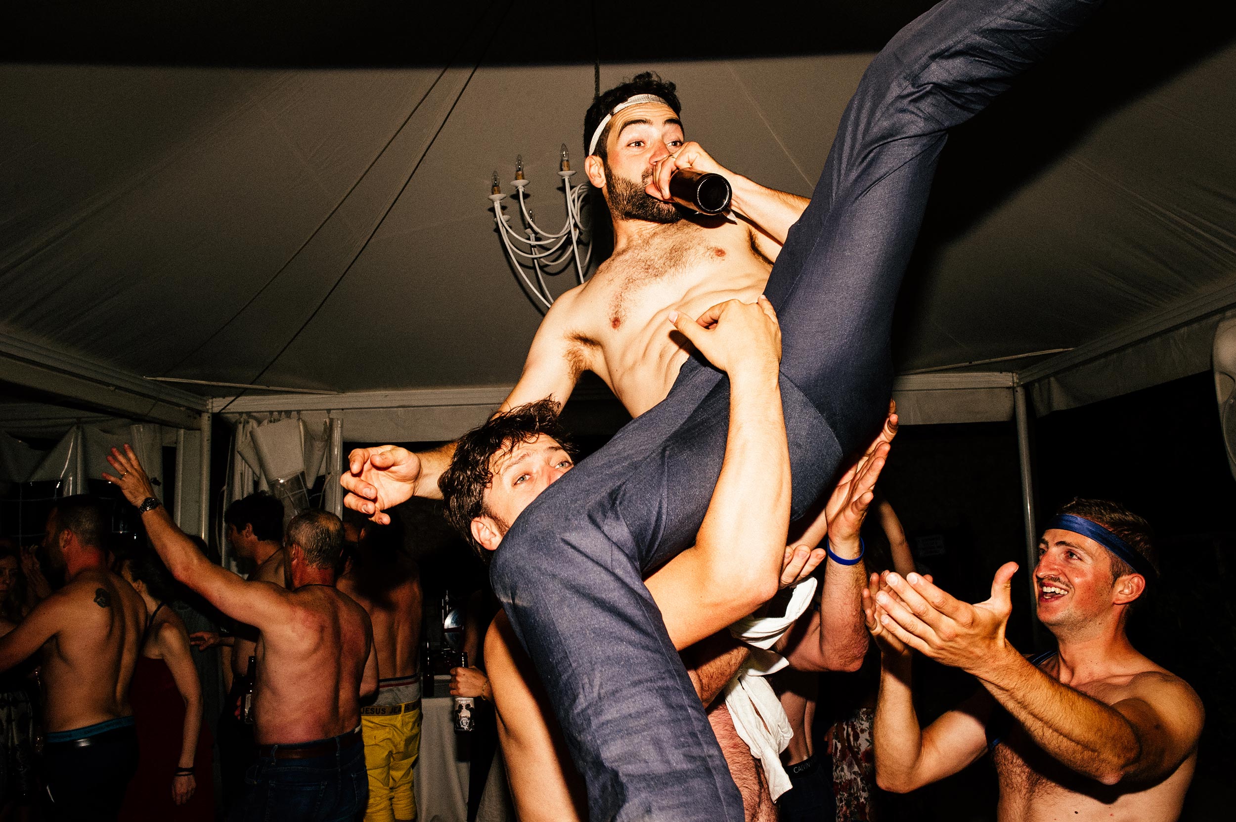 groom being thrown in the air naked while drinking beer during wedding reception dancing