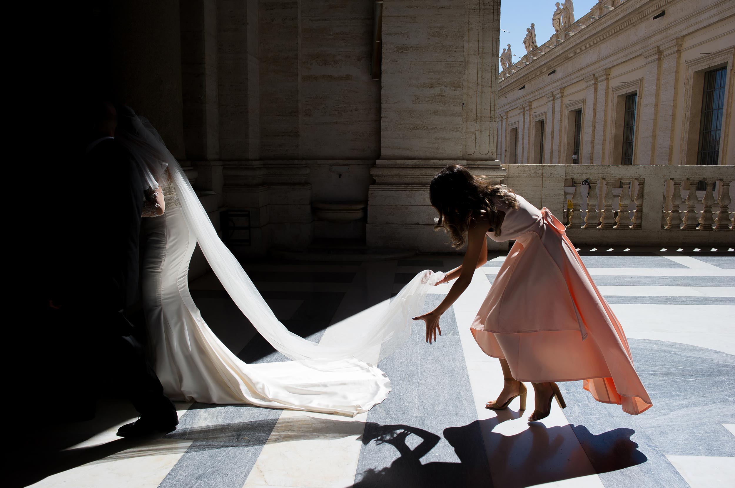 st peter basilica wedding in vatican silhouette bridesmaid helps bride holding the veil