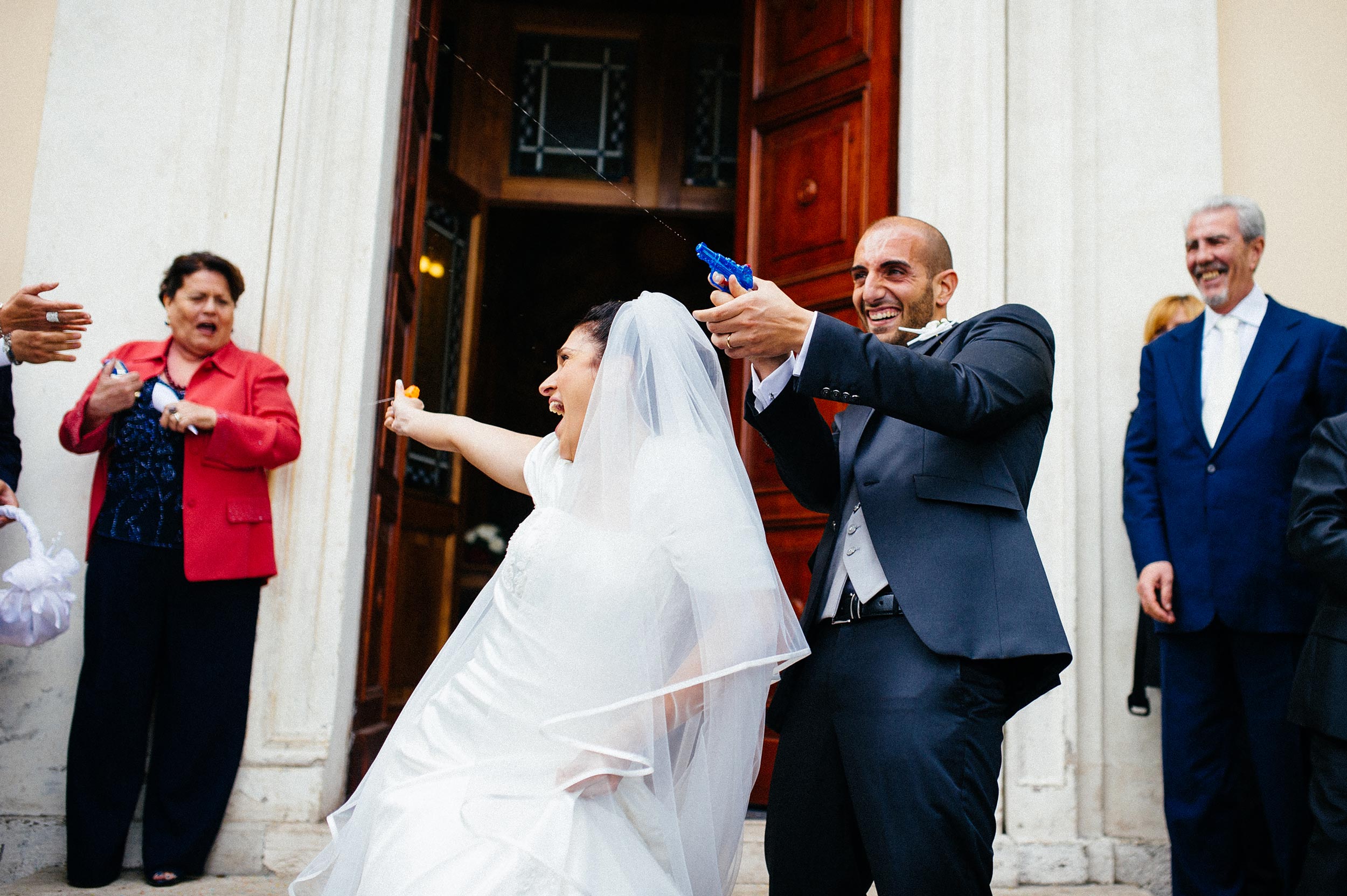 bride and groom outside the church shoot guests with water guns
