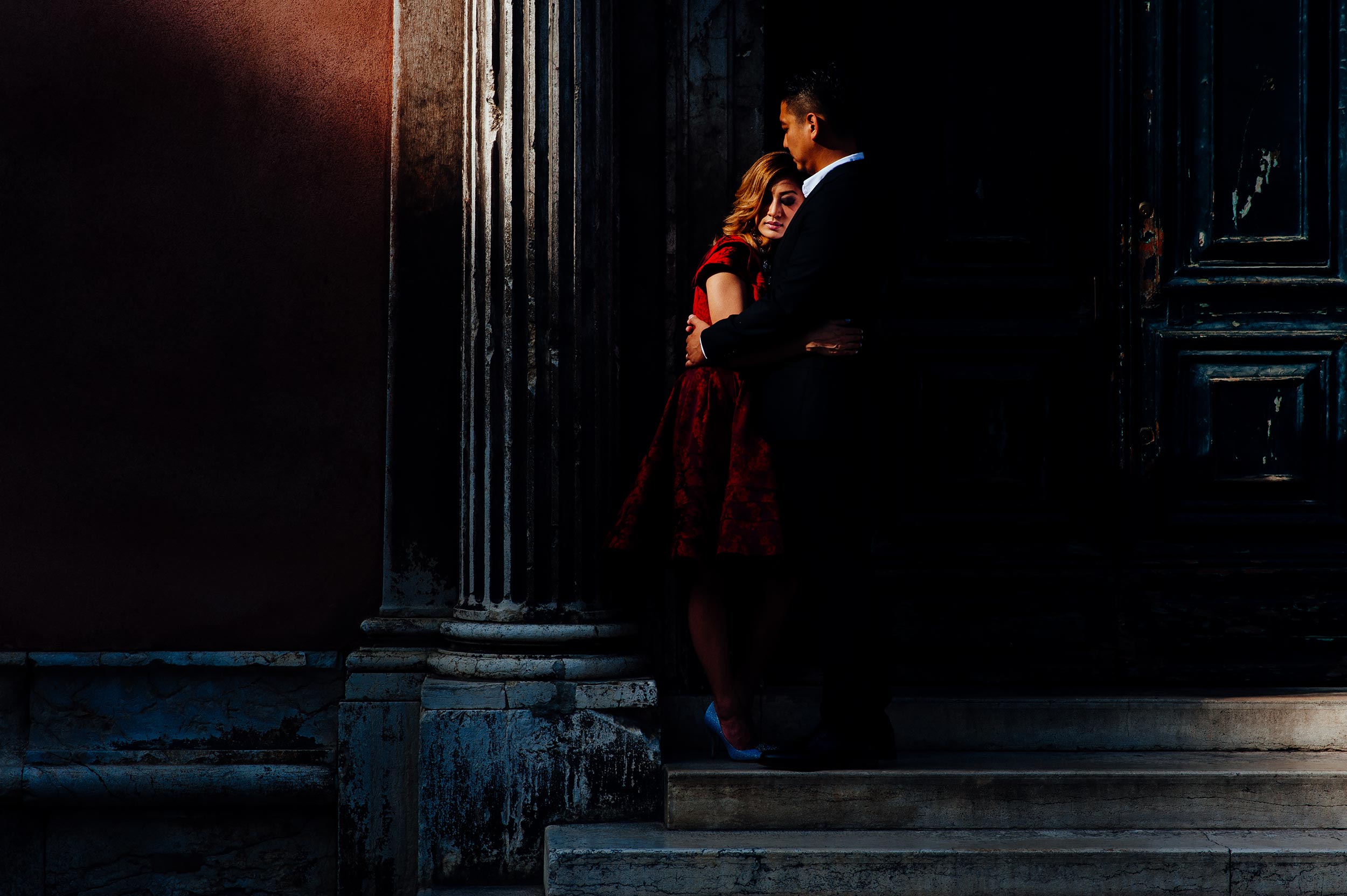 Engagement photographer Venice - couple hugs in ray of light, red dress